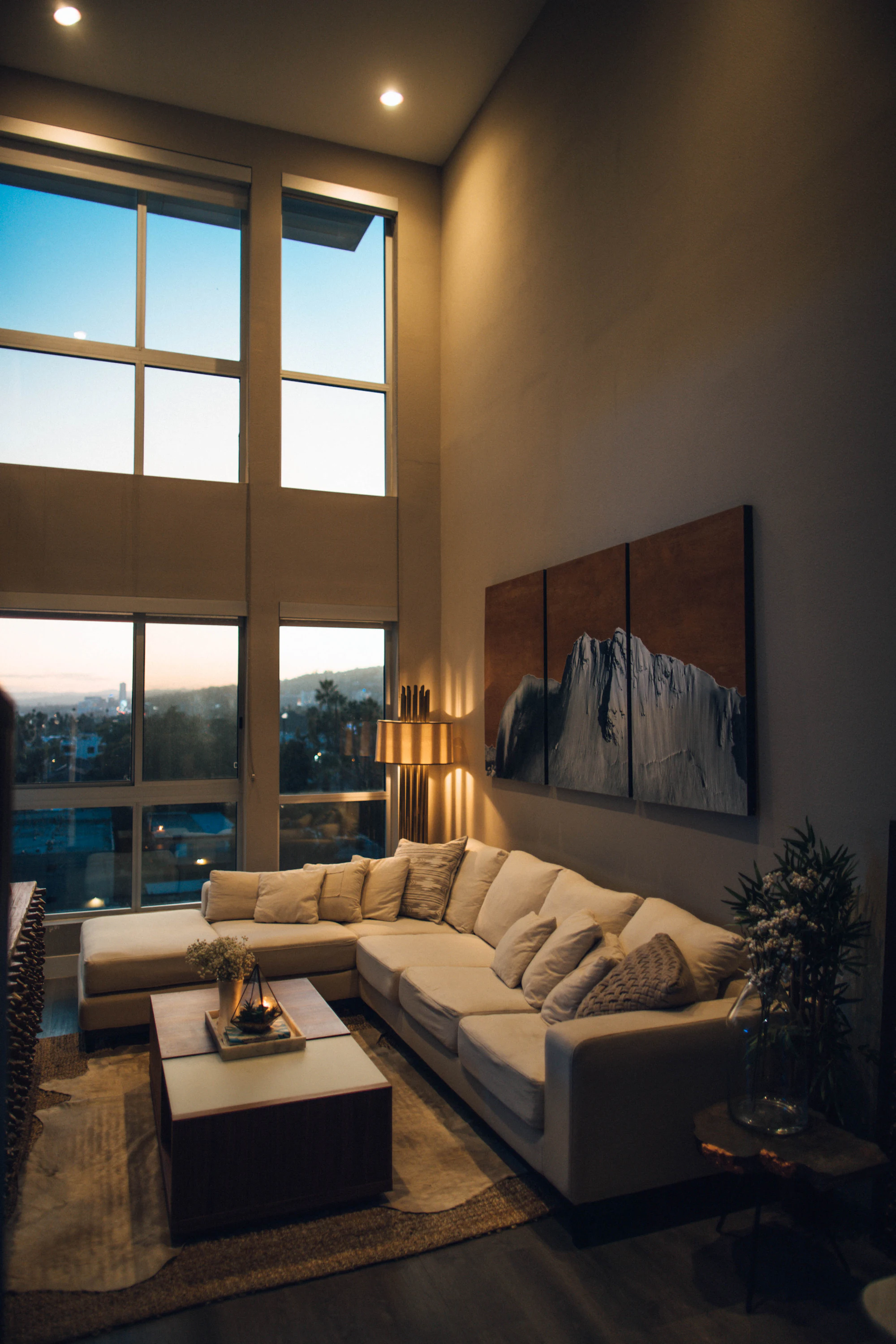 Dramatic double-height lounge with sectional sofa and city views at dusk