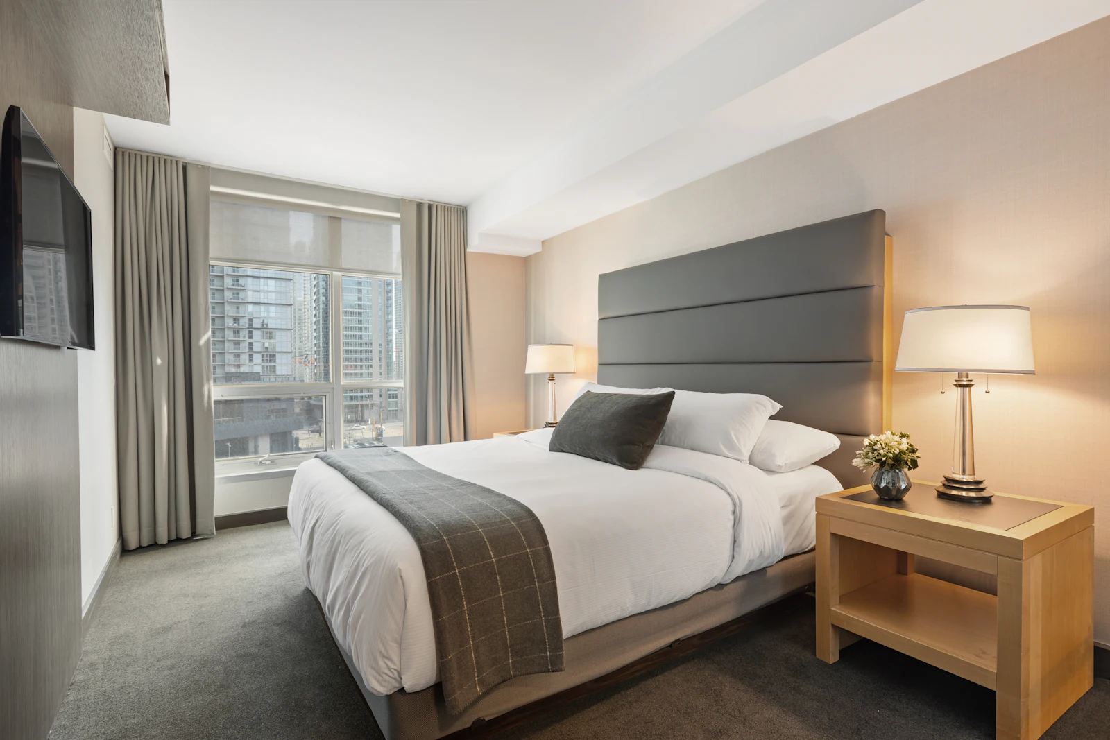Serene bedroom with upholstered grey headboard, bedside lamps and large windows