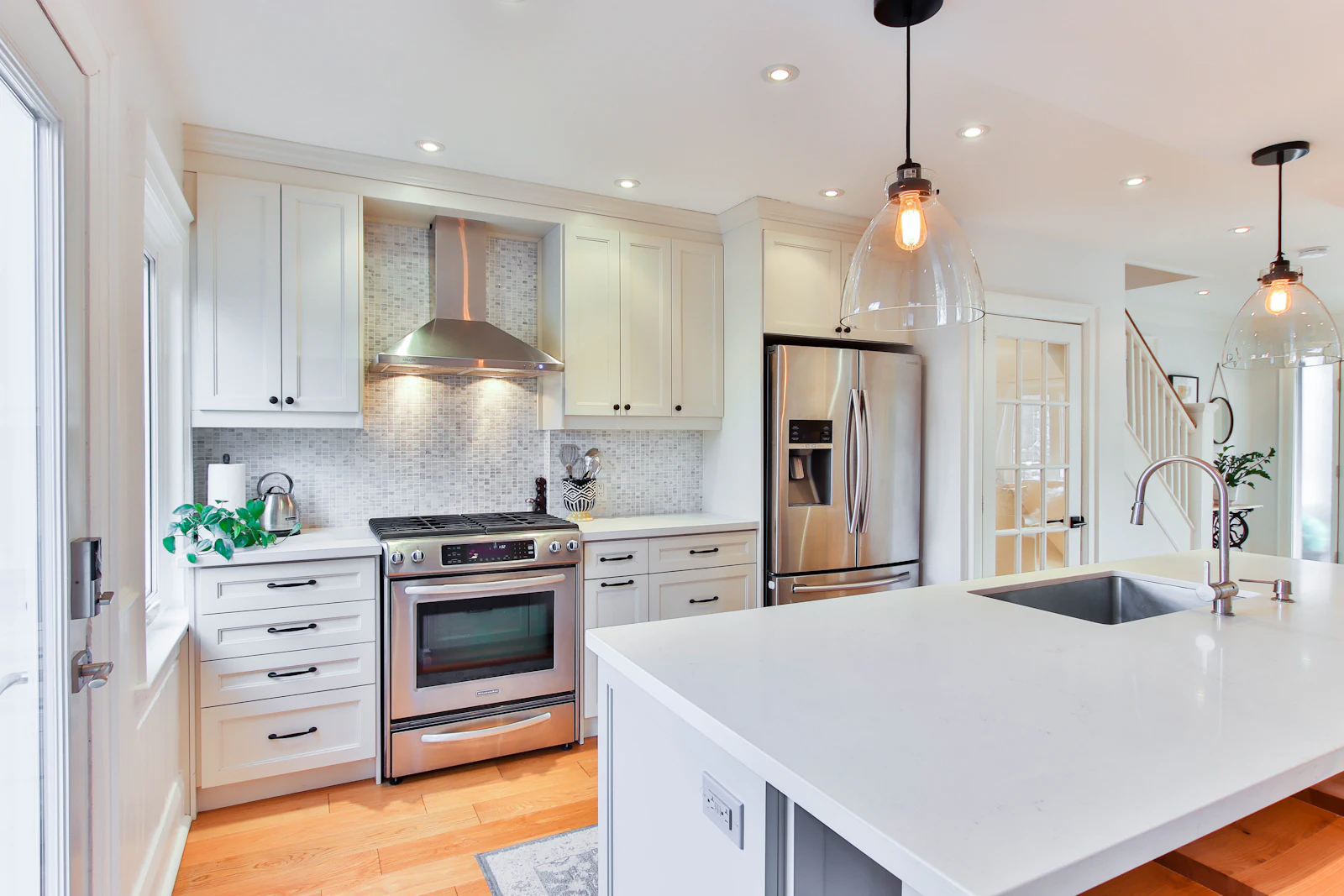 White kitchen with island, stainless appliances and pendant lights
