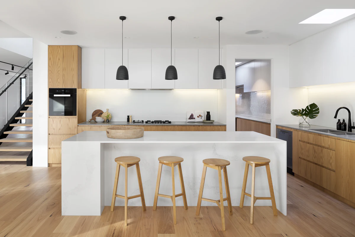 Modern modular kitchen with white island, oak bar stools and black pendant lights
