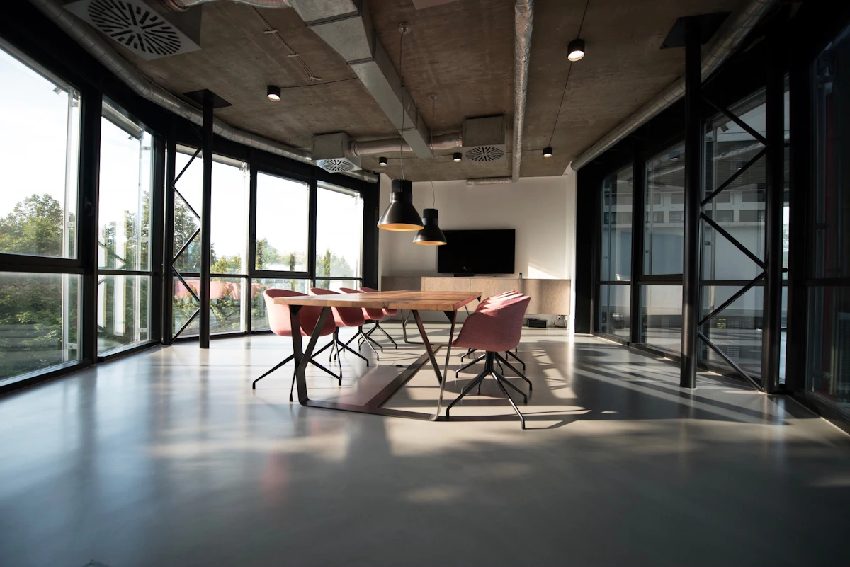 Modern open office interior with glass walls, meeting table and concrete ceiling